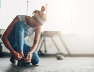 Buy stock photo Defocused shot of a woman tying her shoelaces in a gym
