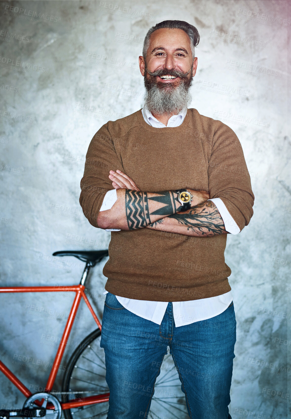 Buy stock photo Portrait of a middle aged man standing with his arms folded with a red bicycle in the back against a grey background