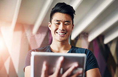 Buy stock photo Low angle shot of a cheerful young man browsing on a digital tablet while standing in the office during the day