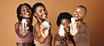 Happy black woman, skincare and beauty products for tone or foundation against a brown studio background. Group portrait of African female people or model smile together with skin makeup on mockup