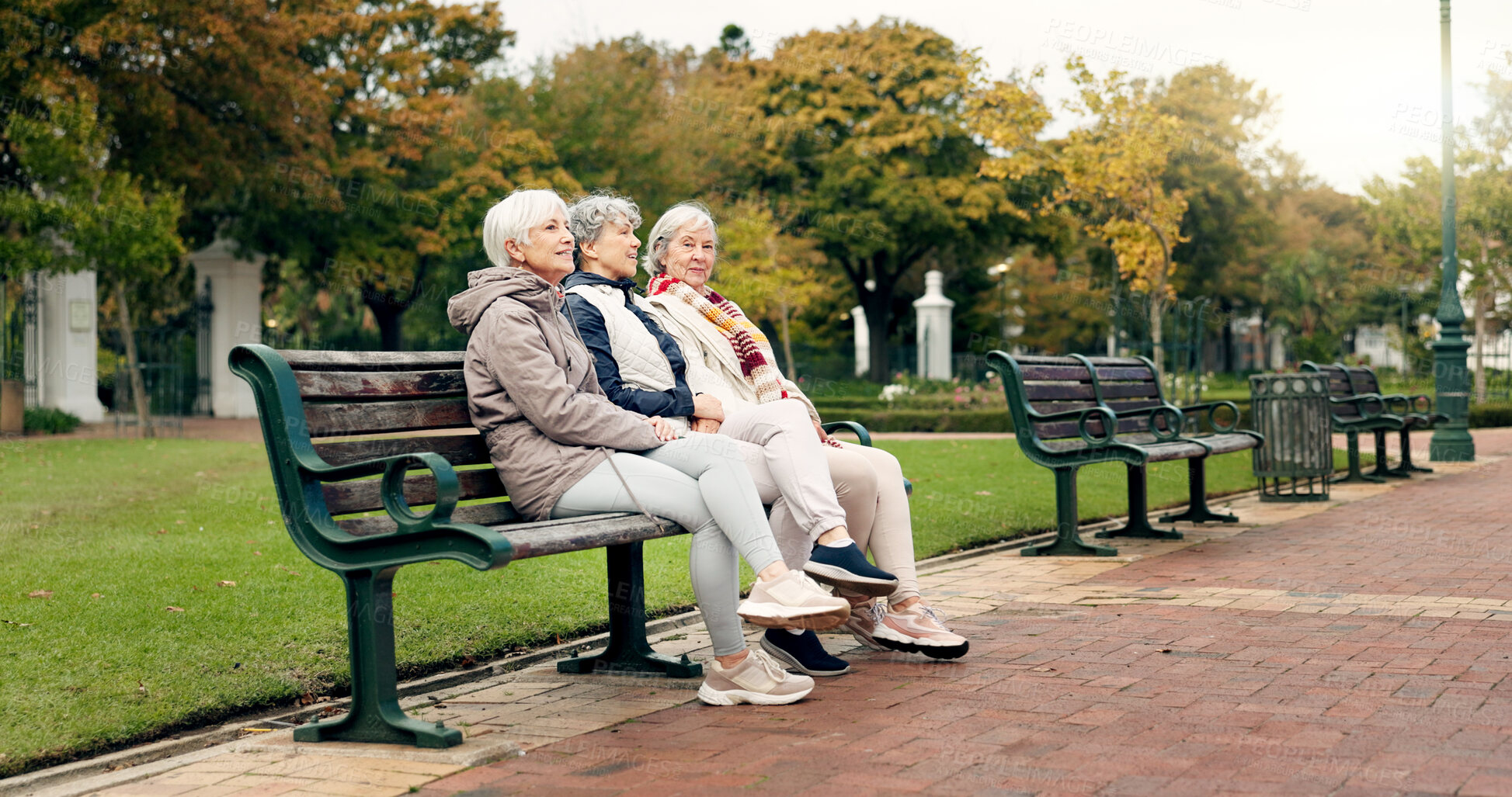 Buy stock photo Happy, senior friends and walking together on an outdoor path or relax in nature with elderly women in retirement. People, talking and sitting for conversation on a park bench in autumn or winter