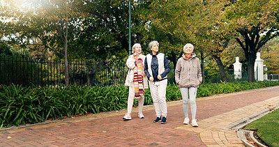 Senior friends, walking and talking together on an outdoor path to relax in nature with elderly women in retirement. People, happy conversation and healthy exercise in the park in autumn or winter