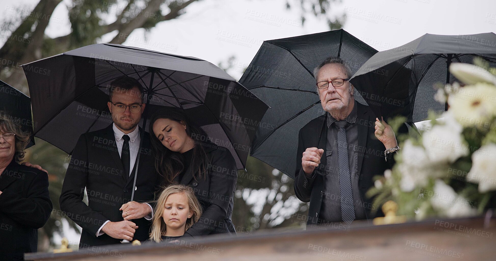 Buy stock photo Death, funeral and umbrella, people at coffin for service in graveyard in respect, mourning and support. Flowers, rain and loss, family at casket in cemetery with memory, grief and grave for burial.