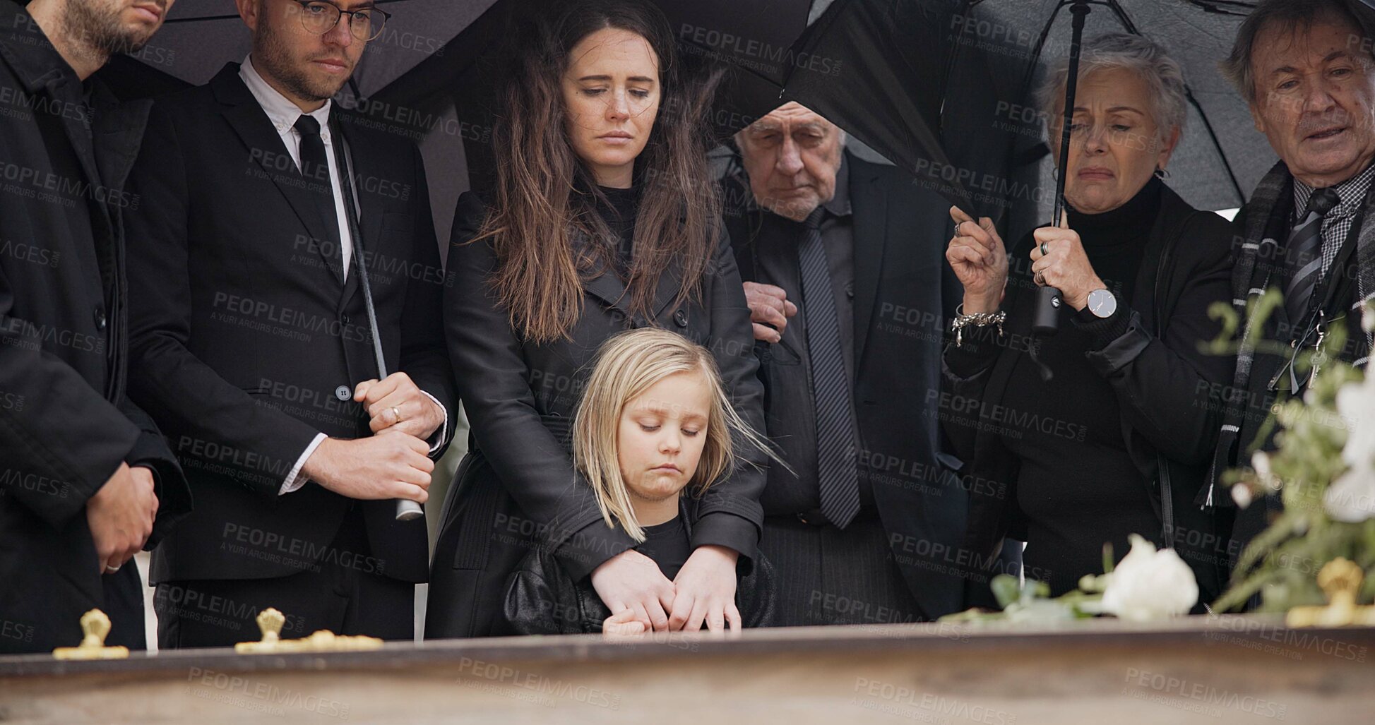 Buy stock photo Loss, grief and people at funeral with umbrella, flowers and coffin, family with sad child at service in graveyard. Roses, death and group in rain at casket in cemetery with kid at grave for burial.