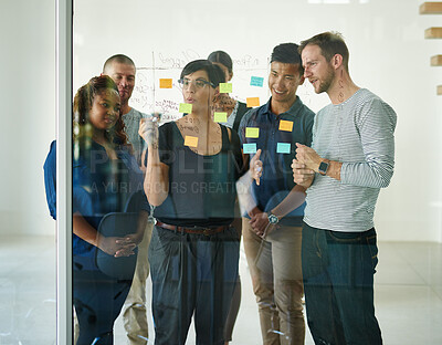 Buy stock photo Group meeting for brainstorming ideas, creative projects or designs using sticky notes on glass wall. Happy and busy interior design team talking about decorating the modern and empty office room