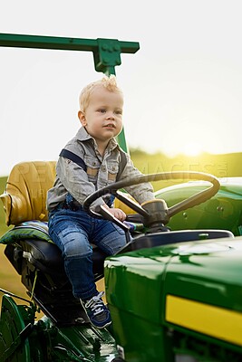 Buy stock photo Shot of an adorable little boy riding a tractor on a farm
