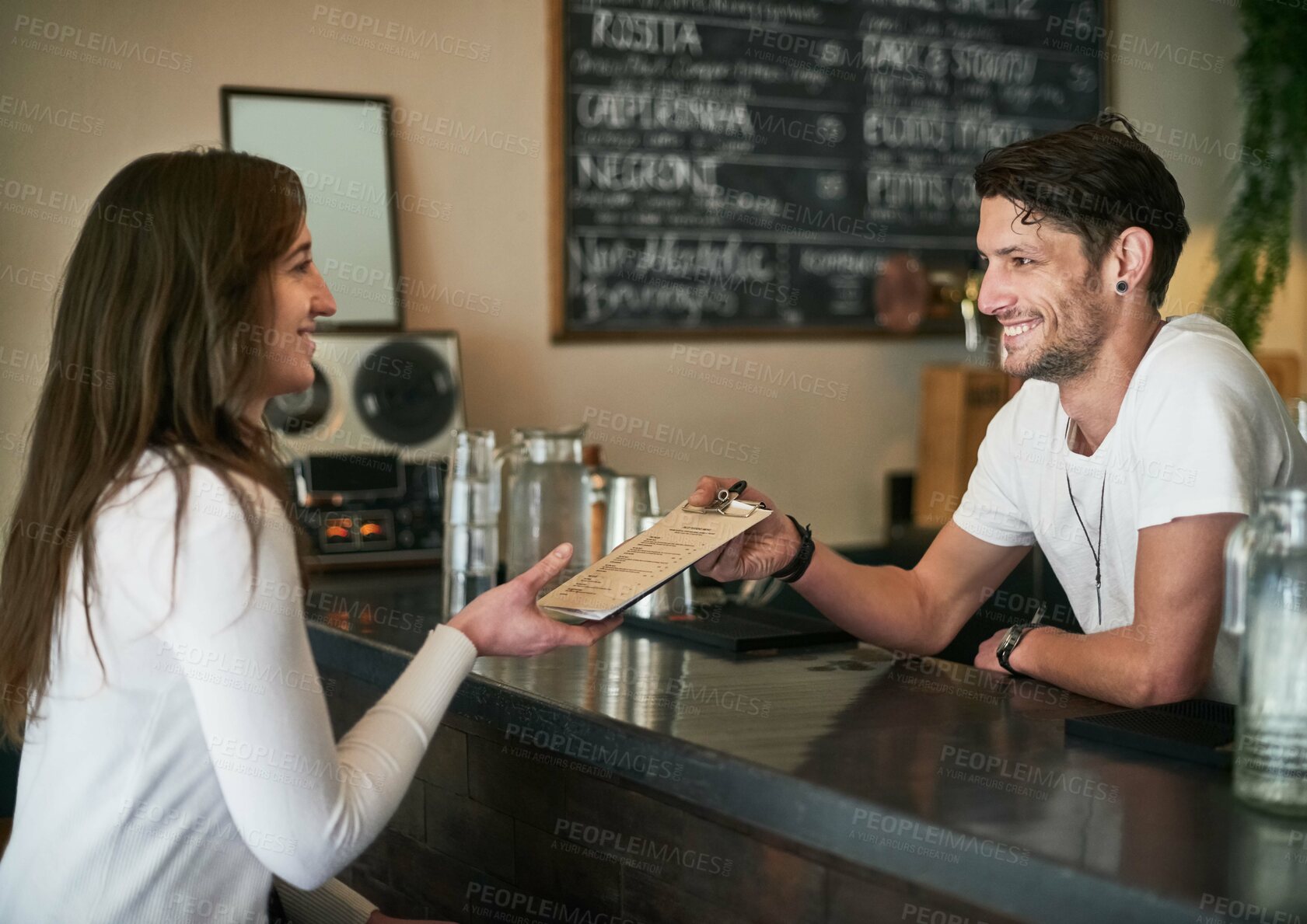 Buy stock photo Shot of a friendly young bartender helping a customer with her order across the bar counter