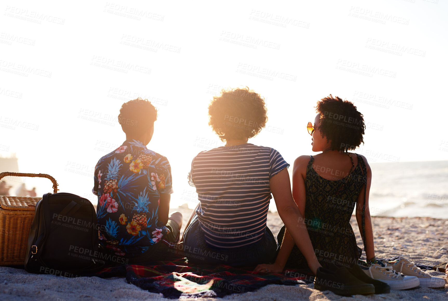 Buy stock photo Rearview shot of an unrecognizable diverse trio of women having a picnic on the beach during the day