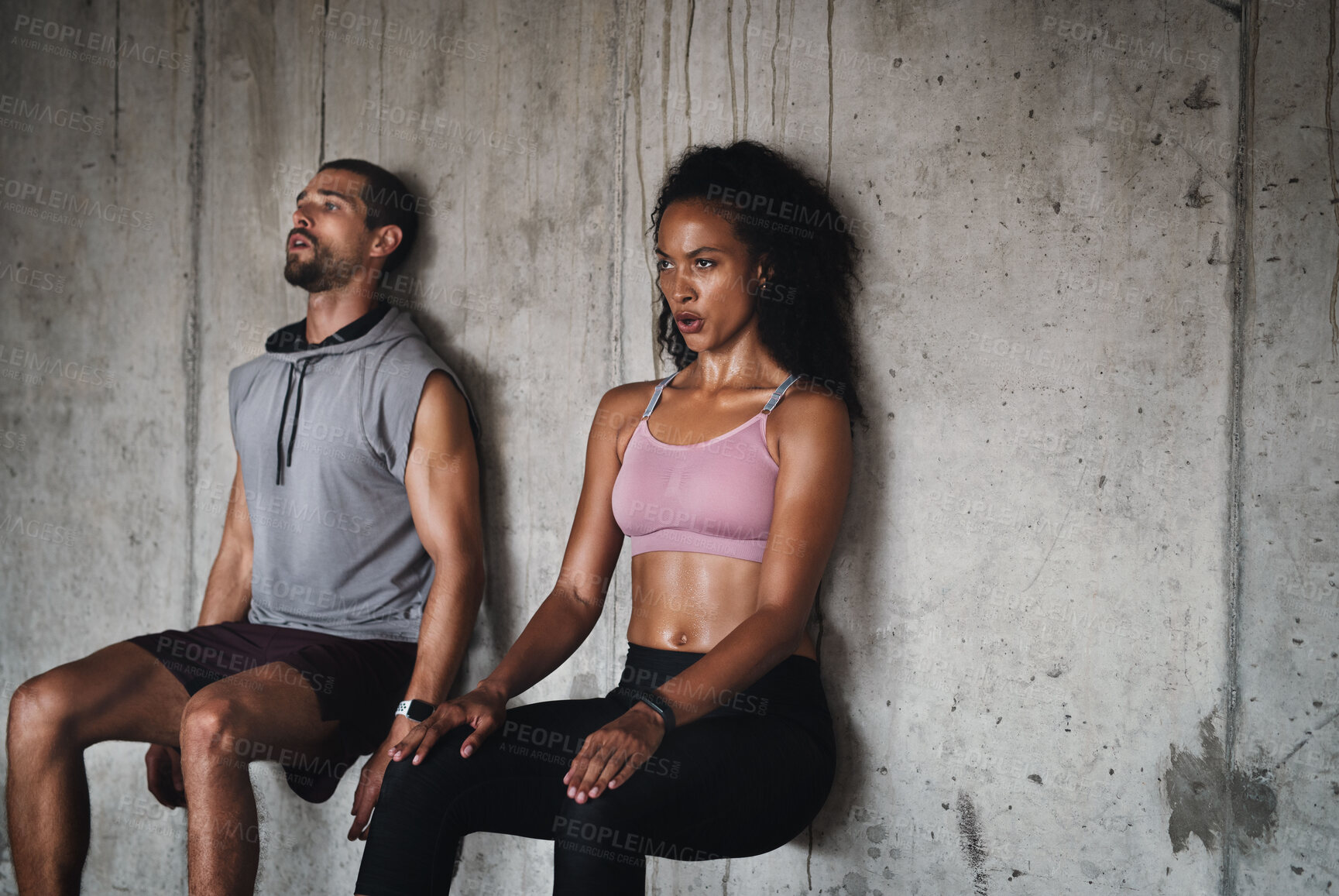 Buy stock photo Shot of a sporty young couple exercising against a wall inside an underground parking lot