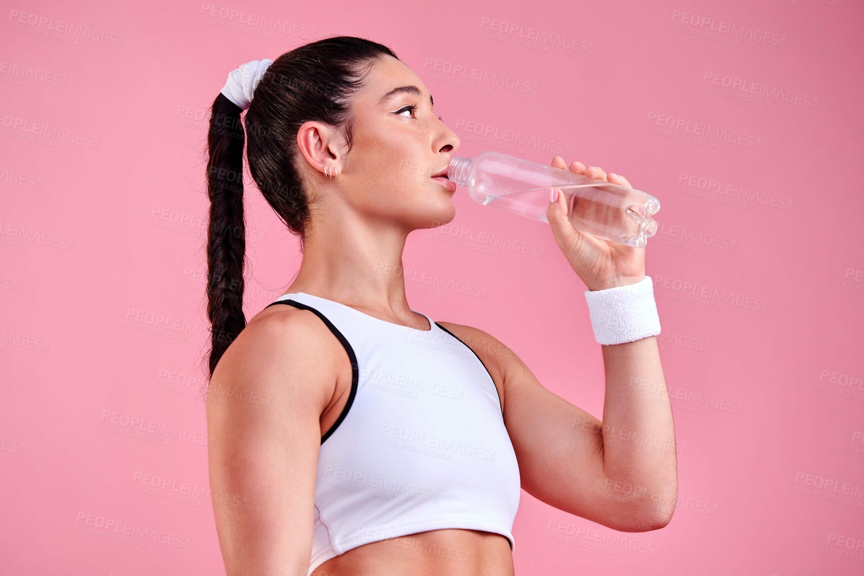 Buy stock photo Studio shot of a sporty young woman drinking water against a pink background