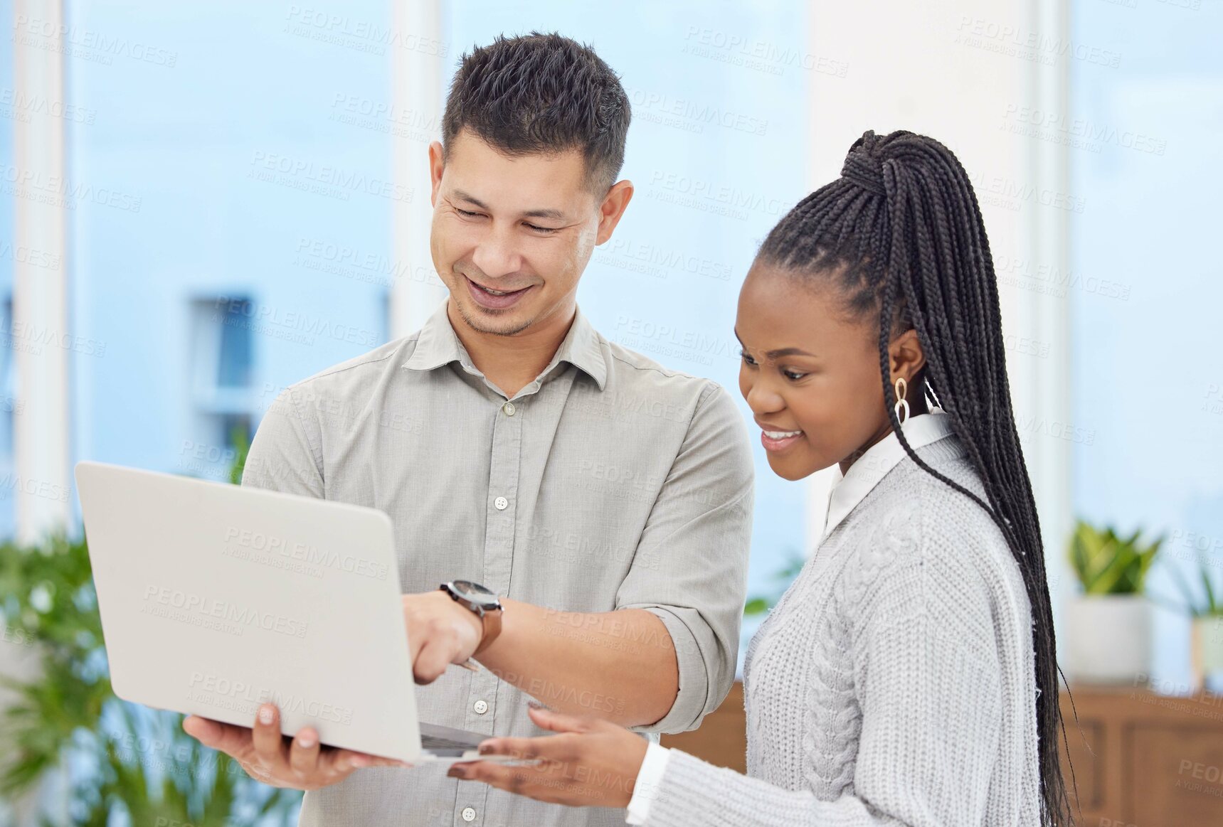 Buy stock photo Shot of two young businesspeople standing together in the office and using a laptop