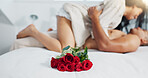 Couple, red roses and lying on bed for anniversary, love or valentines day in romance, embrace or trust at home. Romantic man and woman in bedroom intimacy, passion or bonding with flowers at house