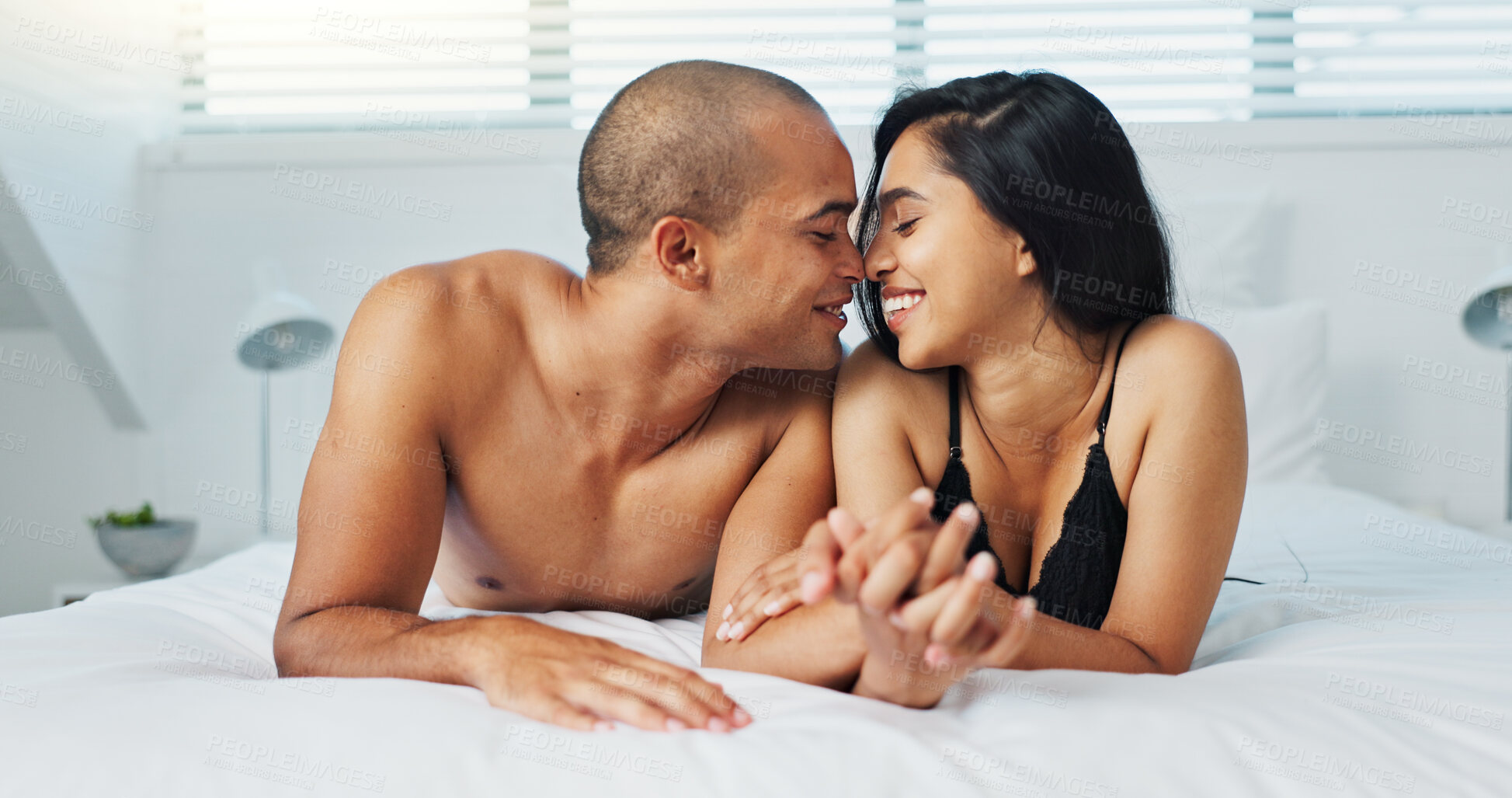 Buy stock photo Happy couple, relax and kissing on bed for intimacy, morning romance or love in embrace, trust or care at home. Young man and woman smile lying in bedroom for passion or bonding together at house