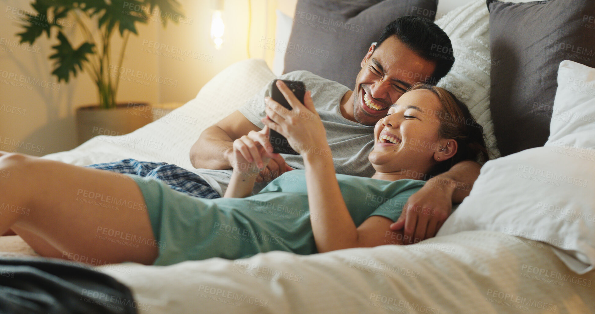 Buy stock photo Asian couple, phone and social media for communication and entertainment on bed to relax, laughing and watch funny videp in bedroom at home. Man and woman using 5g internet while lying together