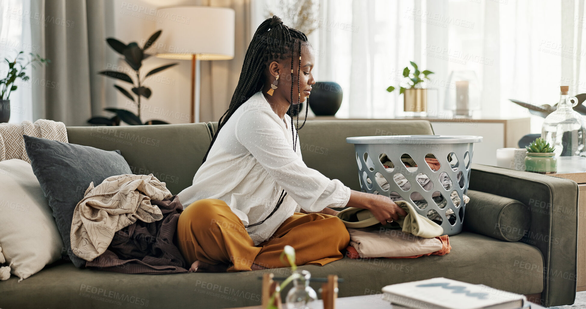 Buy stock photo Laundry, housework and a black woman folding washing on a sofa in the living room of her home to tidy. Smile, relax and a happy young housewife cleaning her apartment for housekeeping or hygiene