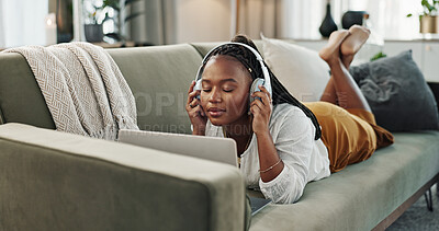 Home, headphones and black woman on a couch, laptop and typing with connection, internet and streaming music. African person, apartment and girl on a sofa, pc and headset with sound, song and audio
