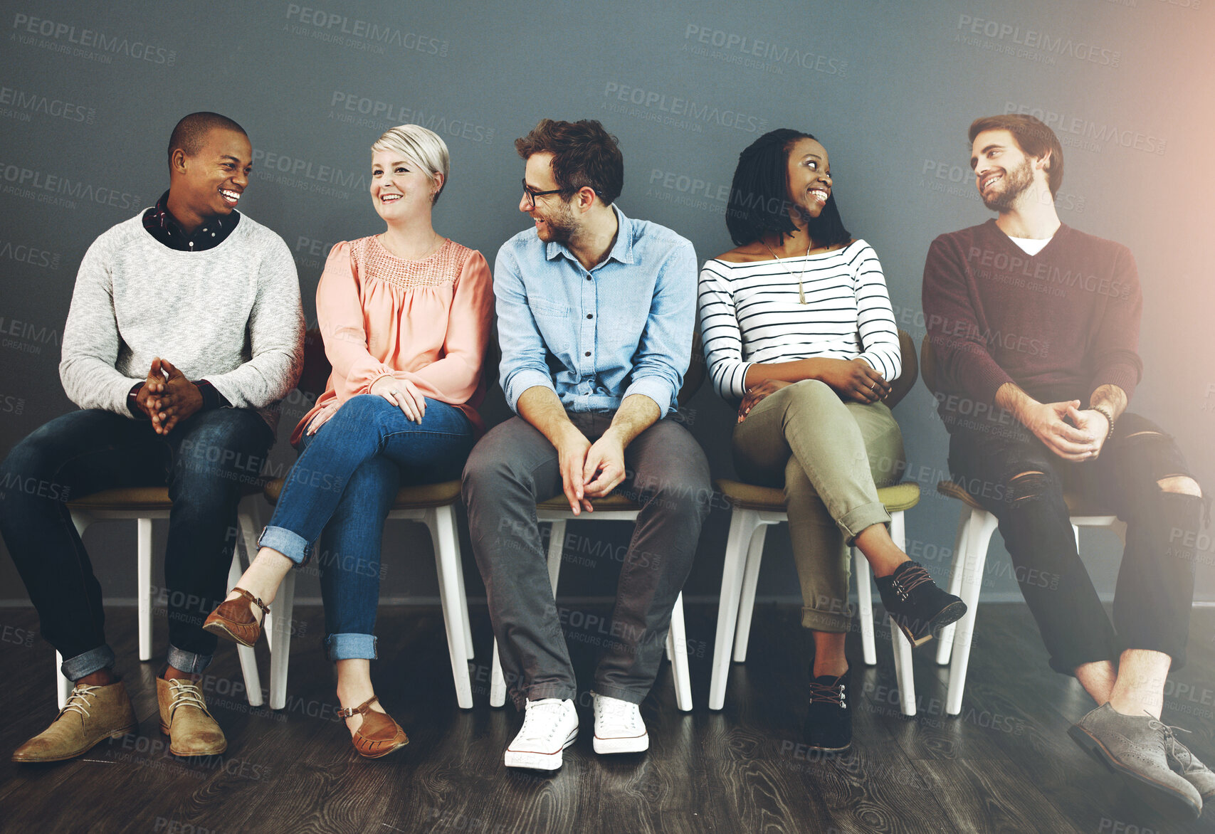 Buy stock photo Studio shot of a group of young people waiting in line on chairs and chatting against a gray background