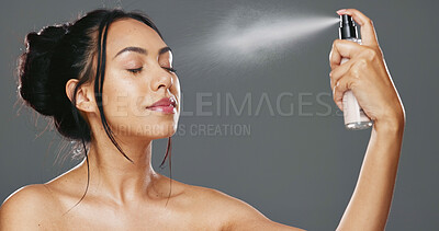 Face, woman and spray after makeup studio with product for mockup in cosmetics on gray background. Female model, happy and smile for beauty, application and facial mist on skin, hydration and glow