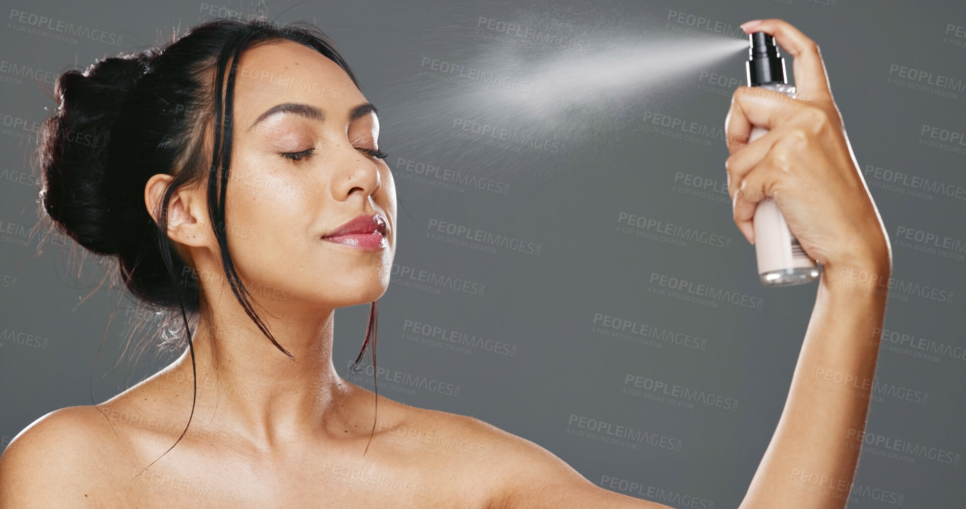 Buy stock photo Face, woman and spray after makeup studio with product for mockup in cosmetics on gray background. Female model, happy and smile for beauty, application and facial mist on skin, hydration and glow