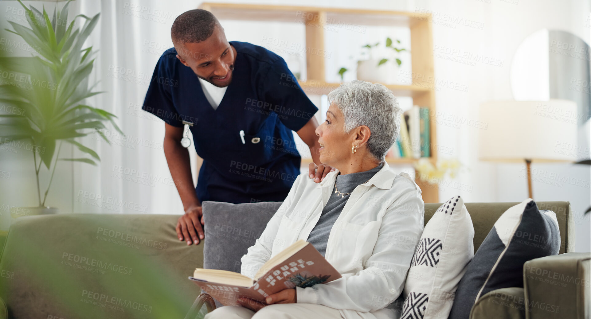 Buy stock photo Elderly, woman and nurse on sofa with support, conversation and caregiver in living room of retirement home. Senior, person and man with kindness, happiness and discussion while reading a book