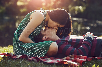 Buy stock photo Shot of an affectionate young couple relaxing together on a picnic blanket in the park