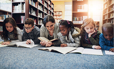 Buy stock photo Shot of a group of elementary school kids and their teacher lying down while working in the library
