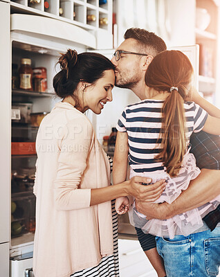 Buy stock photo Shot of a husband lovingly kissing his pregnant wife in the kitchen while holding his daughter