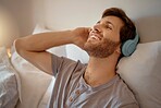 Man listening to music, podcast or radio with headphones at home while relaxing, smile and happy in his bedroom. Peaceful, freedom and young male streaming an online audio playlist enjoying weekend