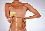 Apple, measuring tape and diet with a black woman in studio on a gray background for weightloss. Food, fitness and health with a female posing to promote exercise, nutrition or health eating