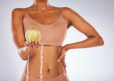 Buy stock photo Apple, measuring tape and diet with a black woman in studio on a gray background for weightloss. Food, fitness and health with a female posing to promote exercise, nutrition or health eating