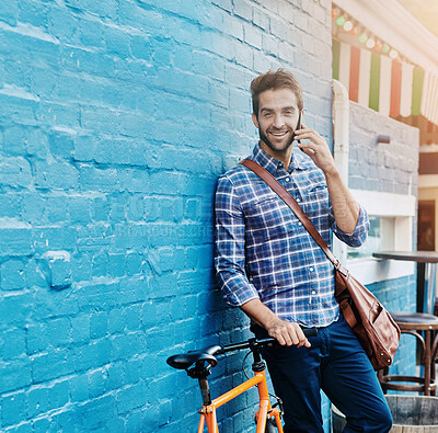 Buy stock photo Shot of a handsome young man leaning against a wall with his bike talking on a cellphone