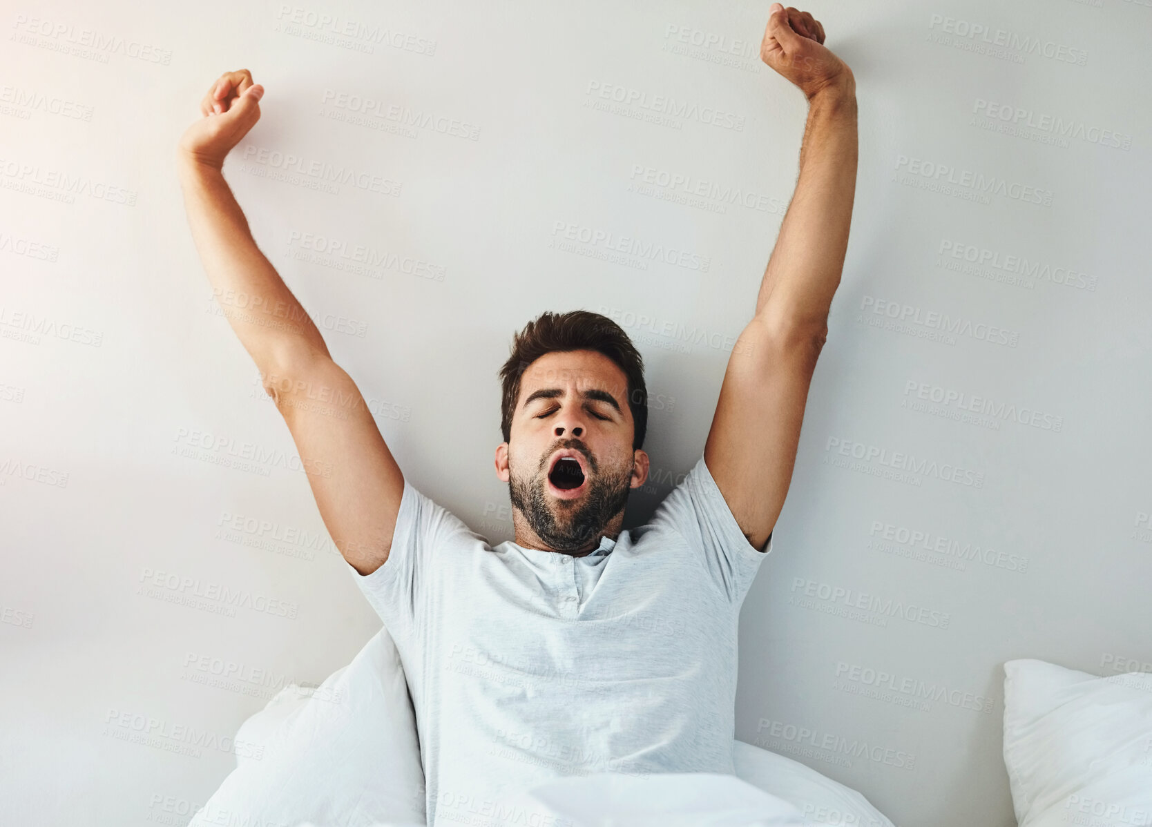 Buy stock photo Cropped shot of a tired young man stretching and yawning after waking up from a good night's sleep