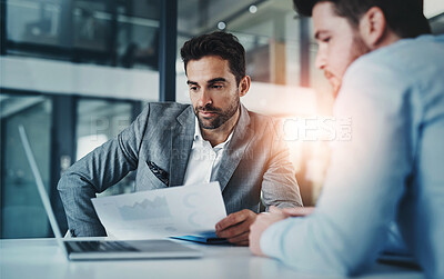 Buy stock photo Shot of two young businessmen using a laptop while going through paperwork together in a modern office