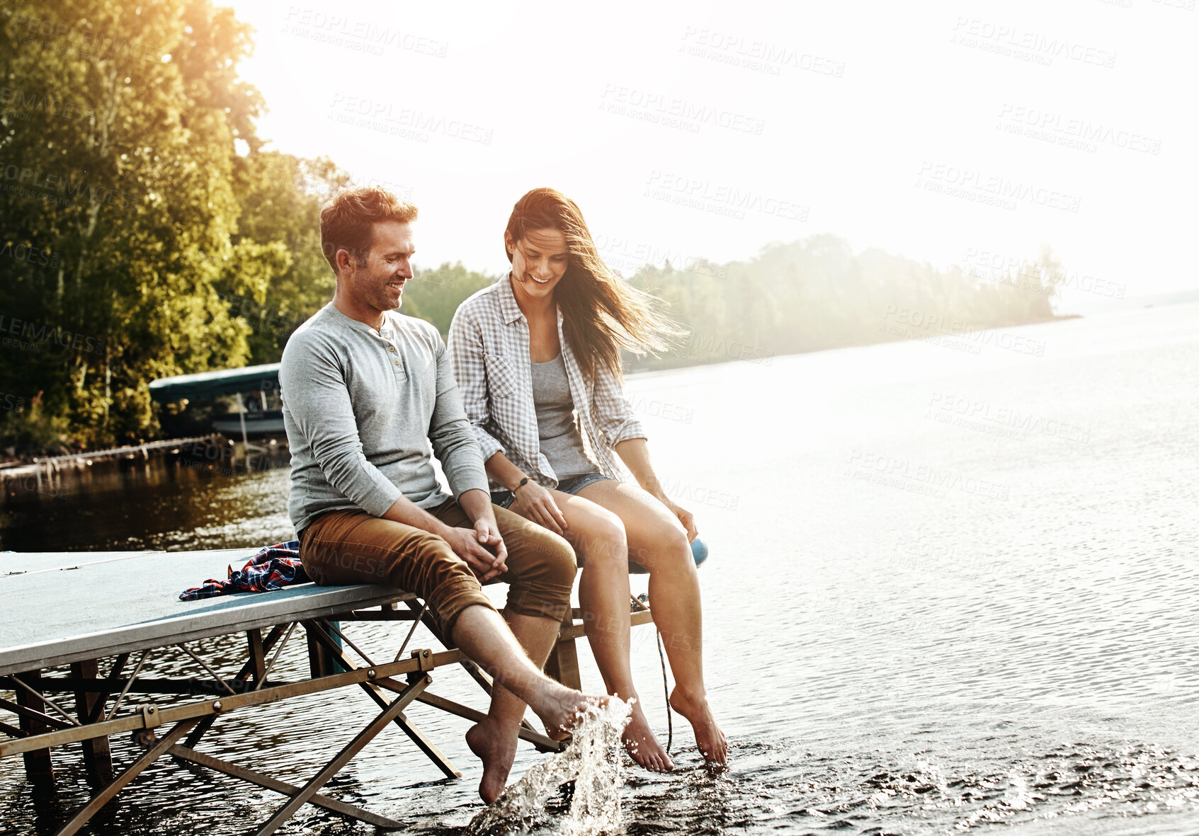 Buy stock photo Vacation, couple and sitting on dock in nature for holiday, fun and splashing feet in water in summer. Happiness, people and romantic getaway by lake for adventure, commitment or love in relationship