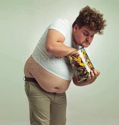 Buy stock photo Candy, sweets jar and man in studio for eating snacks, junk food and dessert in container. Comic, funny and isolated and plus size crazy person with glass for unhealthy diet and sugar on background