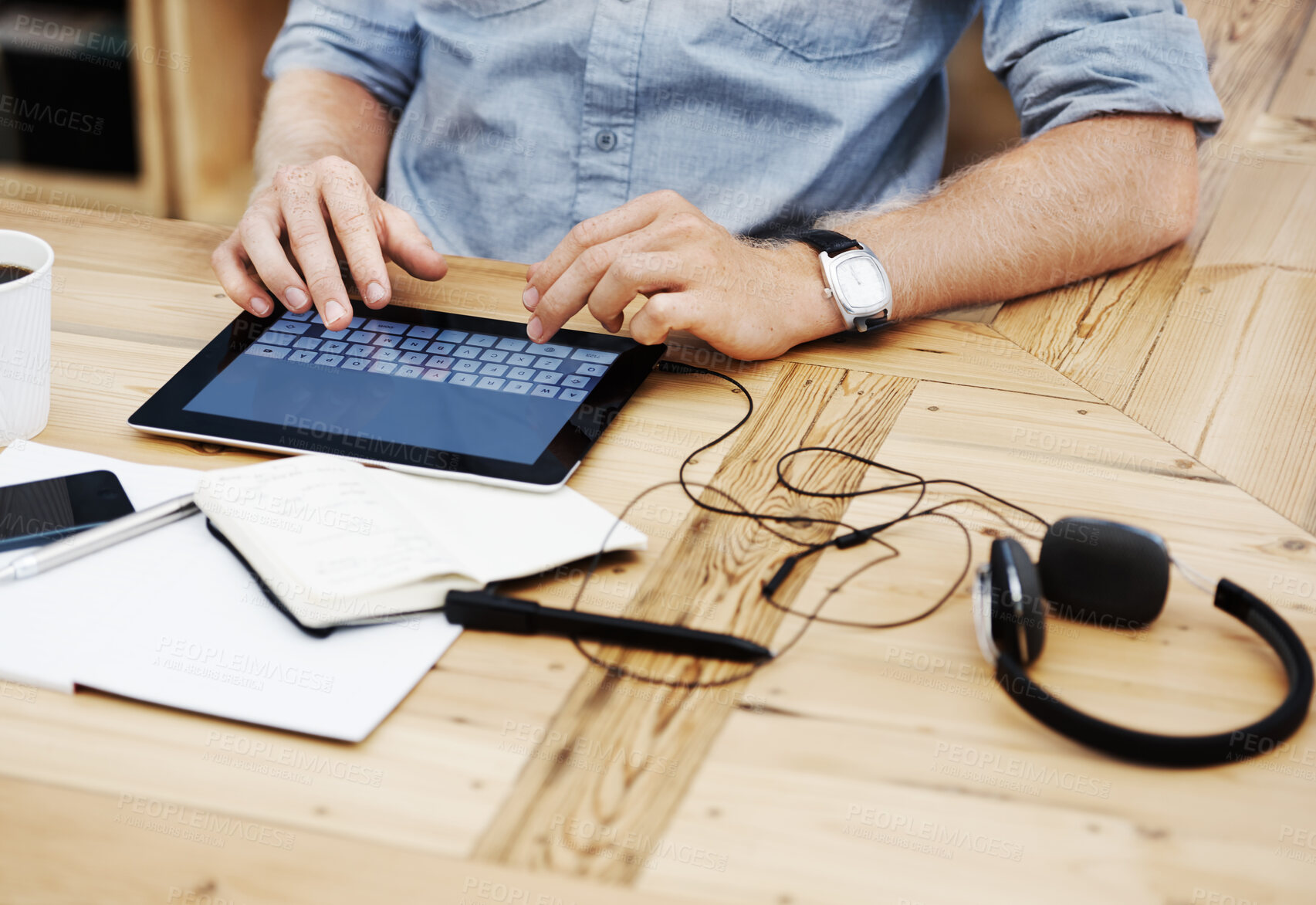 Buy stock photo Closeup of a man typing on a tablet with headphones connected to it inside the office or workplace. Person using a touchscreen device to send an email. Businessman browsing the internet at his desk. 