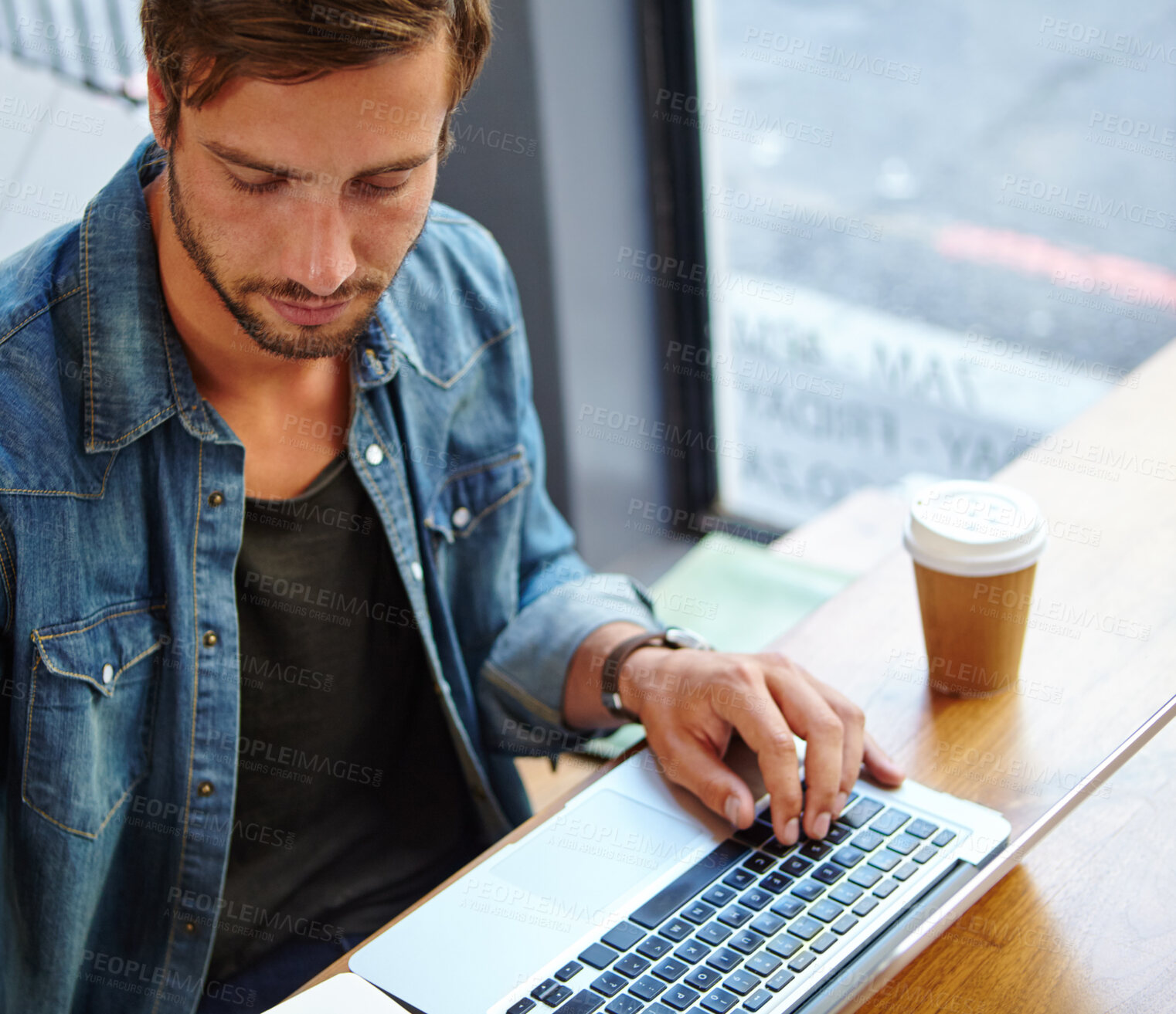 Buy stock photo Shot of a handsome young man working on his laptop in a coffee shop