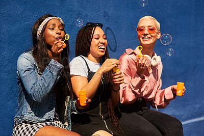 Buy stock photo Happy, friends and women blowing bubbles on vacation, holiday travel or bonding activity and against a blue wall. Happy, game and ladies playing with soap or wand toy or in freedom and social break