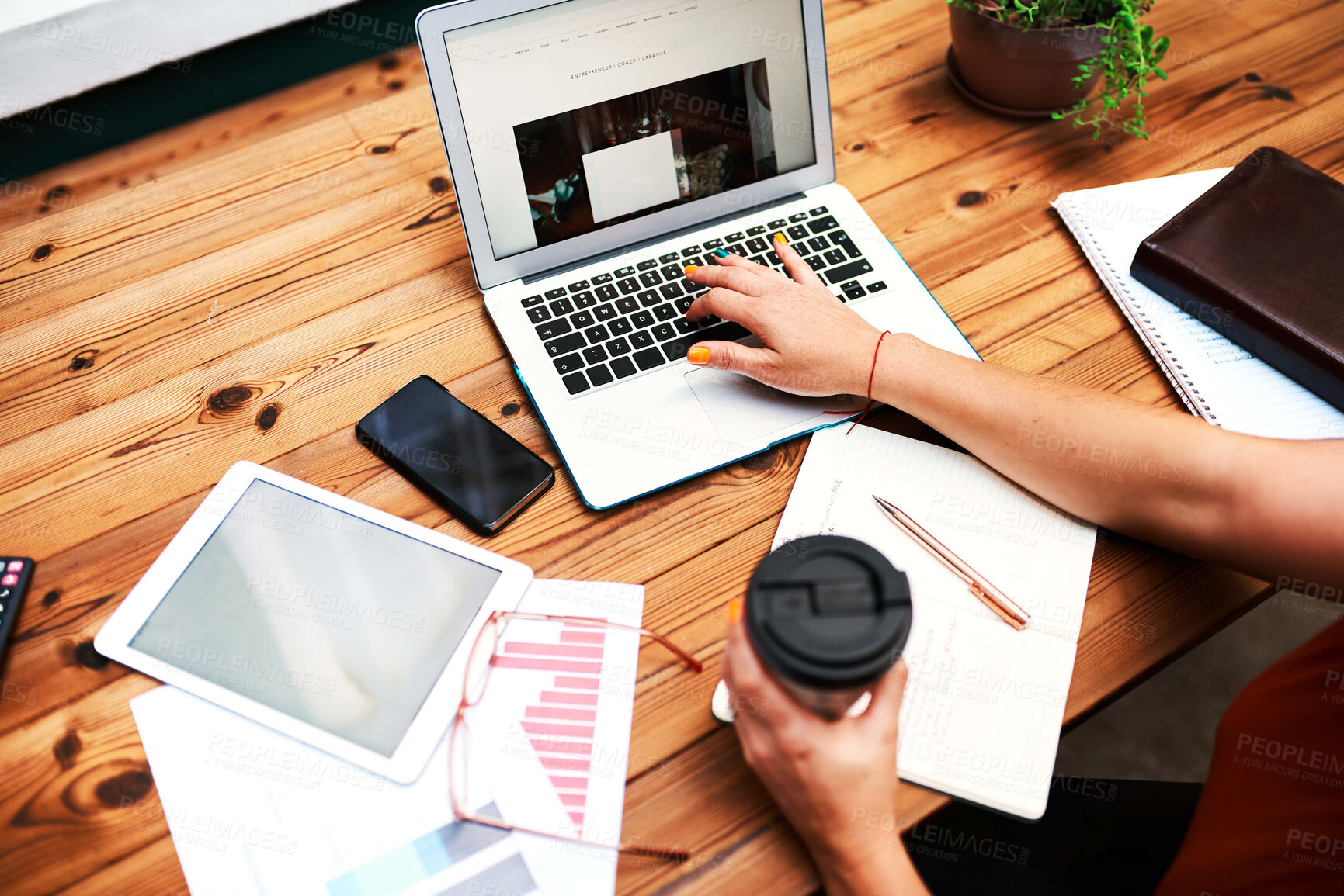 Buy stock photo Cropped shot of an unrecognizable businesswoman sitting alone and using her laptop while holding a cup of coffee