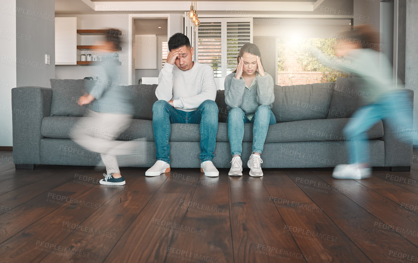 Buy stock photo Shot of two young parents looking tired while their children run around at home