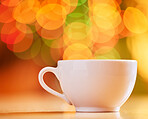 Closeup of teacup isolated on a colourful and vibrant bokeh background. Concept of one white coffee cup on a table in a room indoors. A warm drink or hot tea or coffee served in crockery at home