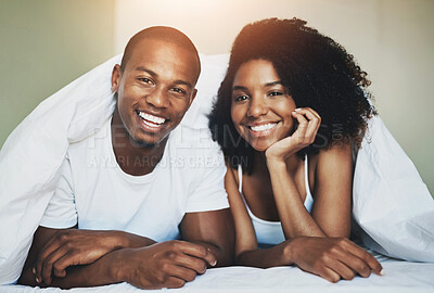 Buy stock photo Portrait of a happy young couple relaxing under a duvet in their bedroom