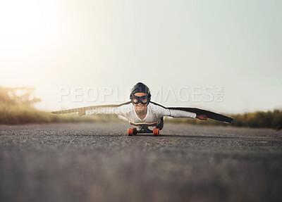 Buy stock photo Portrait of a young boy pretending to fly with a pair of cardboard wings while riding a skateboard outside