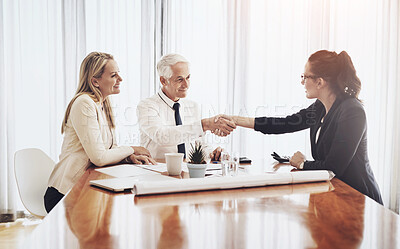 Buy stock photo Shot of a group of architects working together on blueprints of a house around a table while shaking hands in agreement inside of a building