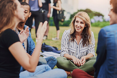 Buy stock photo Shot of a group of young students studying together while being seated in a park outside during the day