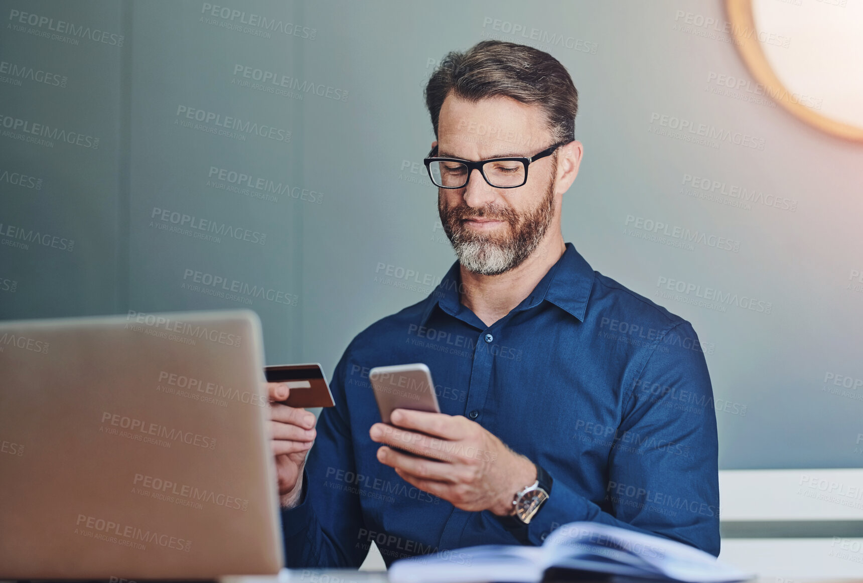 Buy stock photo Shot of a cheerful middle aged businessman working on his laptop and paying bills with his credit card at home during the day