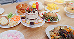 Birthday cake, table and lunch for event, celebration and party on patio with food for meal. Dessert, home and outdoor with feast, vegetable and sweet baking with cupcake and sugar snack on a plate