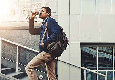 Buy stock photo Shot of a young businessman drinking coffee while walking through the city