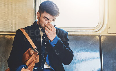 Buy stock photo Shot of a irritated looking young man blowing his nose while being seated inside of a train to get to work