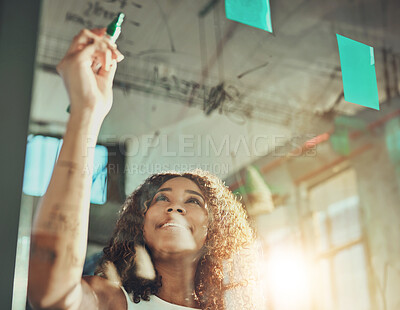 Buy stock photo Shot of a focussed young businesswoman putting up sticky notes on a glass wall while brainstorming in the office at work